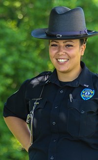 Une femme agent pénitentiaire sourit à la caméra avec des arbres en arrière-plan.
